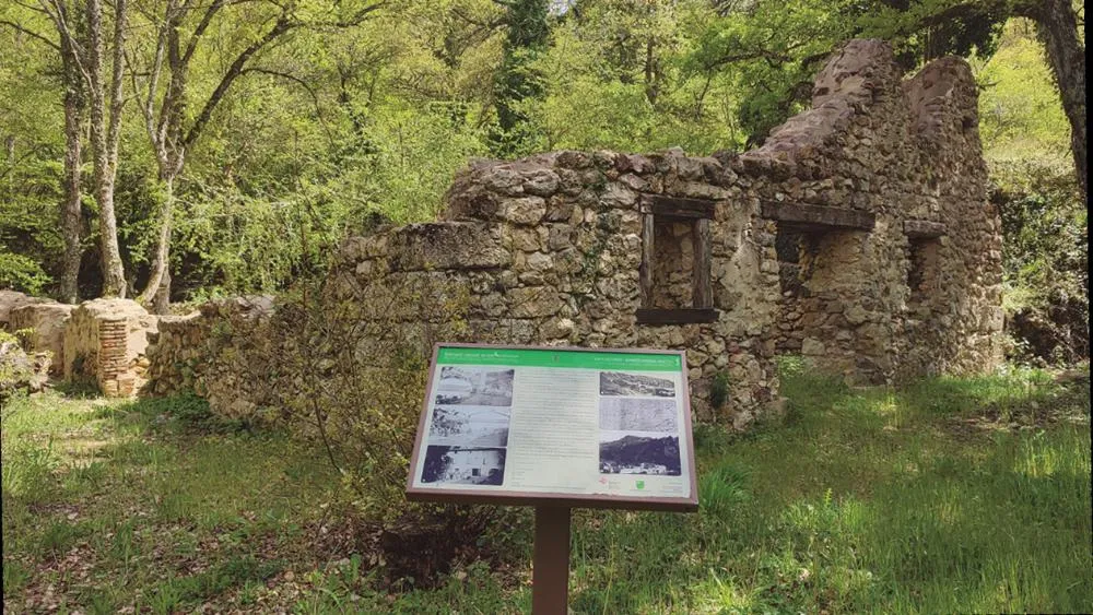 Ruinas de piedra de una antigua fábrica de asfalto en el bosque, con un panel interpretativo de la ruta